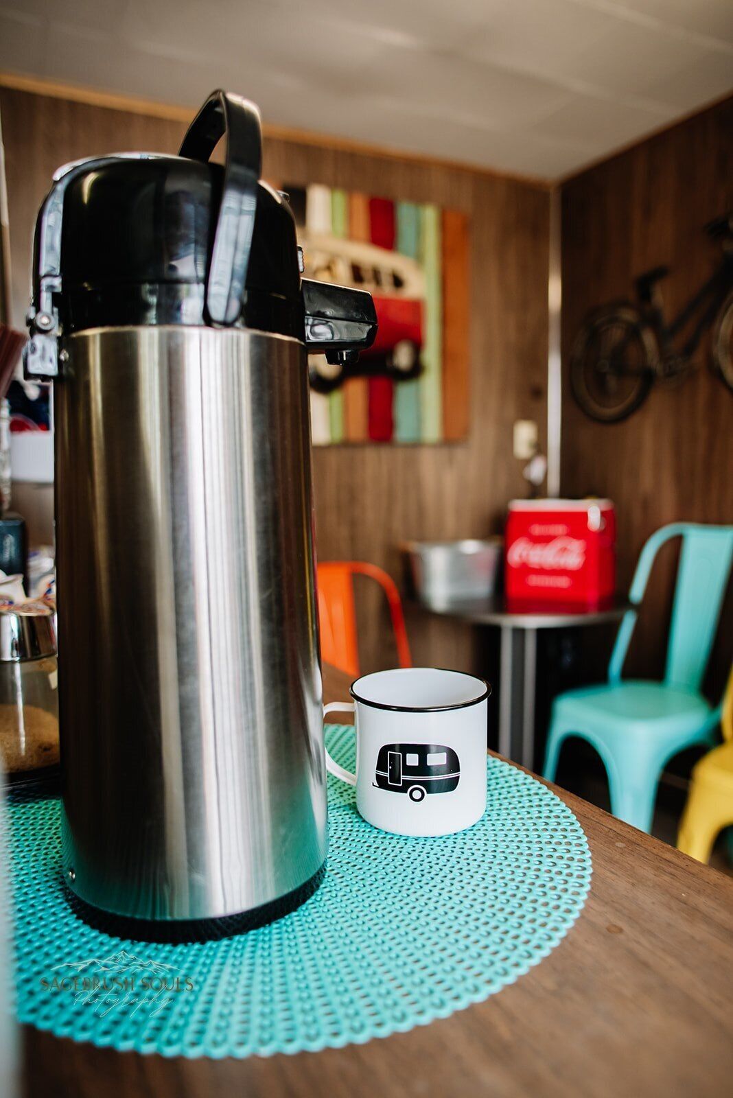 A stainless steel thermos on a wooden table with a white mug featuring a bus design.