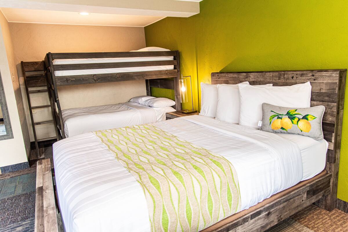 A room with a bunk bed, a single bed, and a nightstand with a lamp.