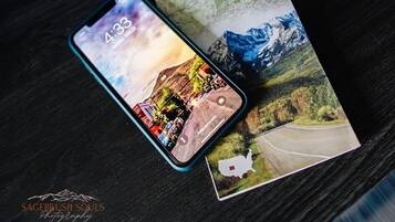 Un teléfono inteligente mostrando una imagen panorámica, un mapa turístico de Colorado y un teléfono giratorio antiguo sobre una superficie de madera.