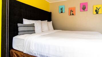 Una cama con ropa de cama blanca, cabecera negra y un banco cubierto de tela marrón.