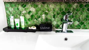 A bathroom vanity with a green mosaic backsplash, a black soap dish labeled "Makeup," and three green bottles of shampoo and conditioner.