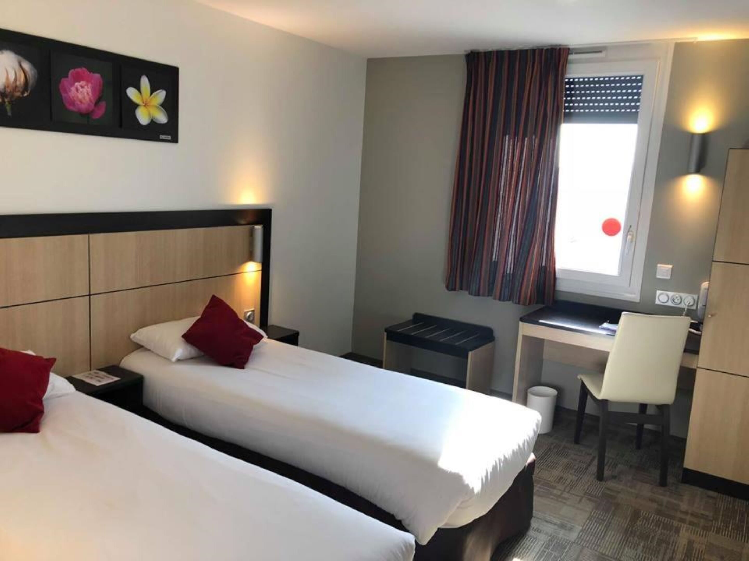Habitación de hotel con dos camas, un escritorio, una silla y un ventanal con cortinas.