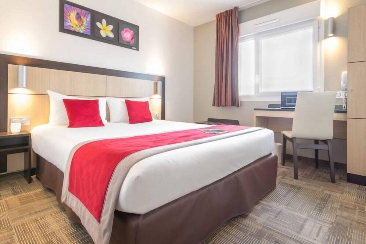 A hotel room with a large bed, a desk, a chair, and a window with curtains.