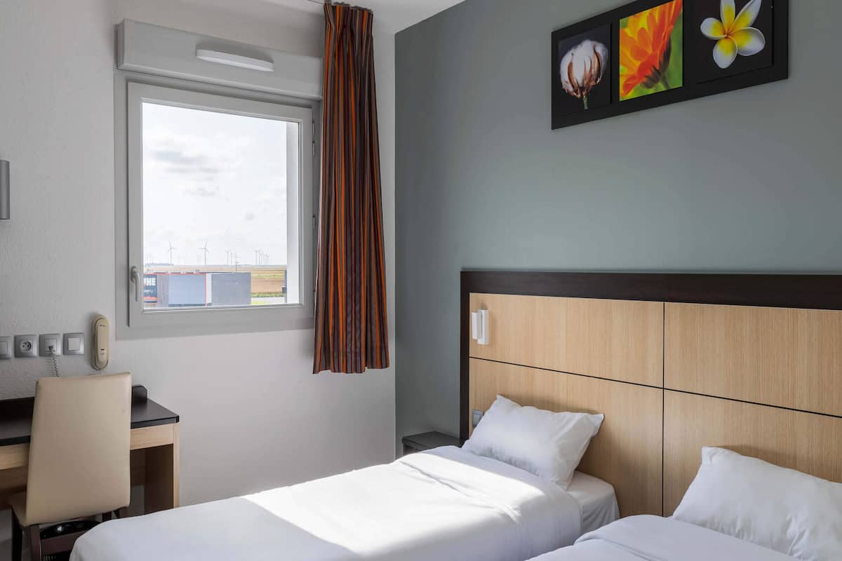 A hotel room with a bed, a desk, and a window with curtains.