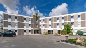 A modern hotel building with a B&B sign, a parking lot, and a clear blue sky. - B&B HOTEL Romilly-sur-Seine (Maizieres-la-Grande-Paroisse)
