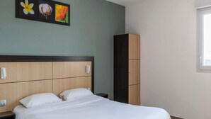 A neatly made bed in a hotel room with a wooden headboard, a small bedside table, and a wardrobe. - B&B HOTEL Romilly-sur-Seine (Maizieres-la-Grande-Paroisse)