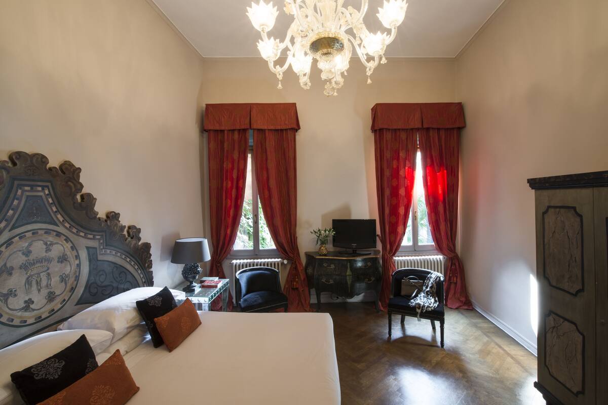 A hotel room with a large bed, two chairs, a television, and a chandelier.