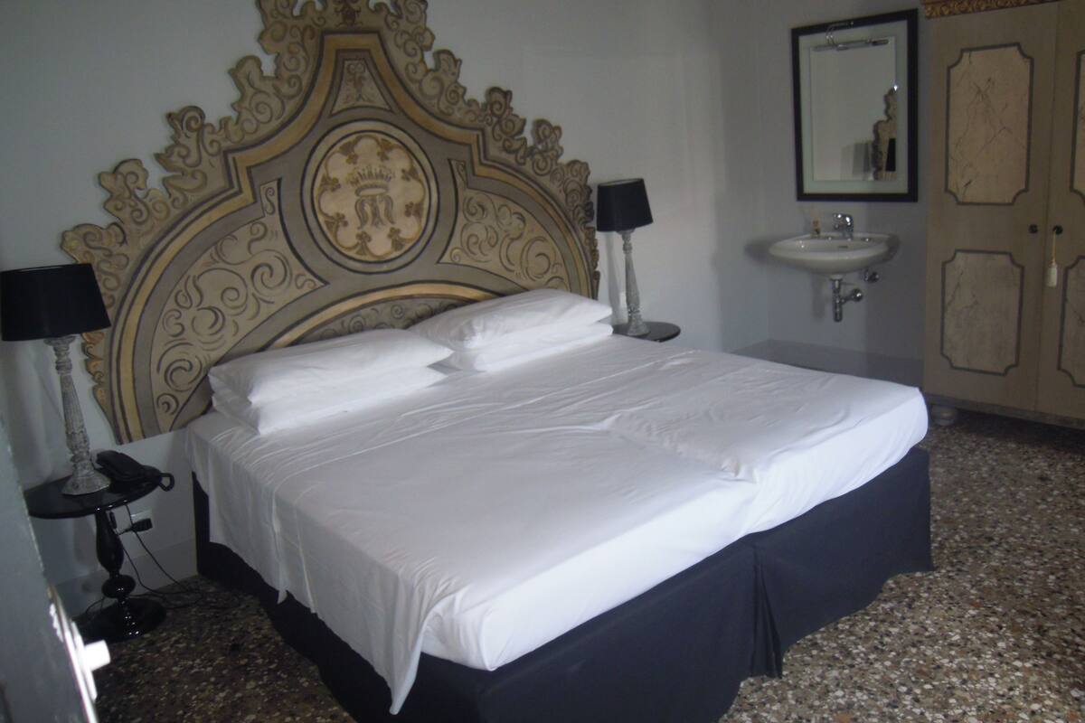 A hotel room with a large bed, two bedside lamps, a wall-mounted mirror, and a sink.