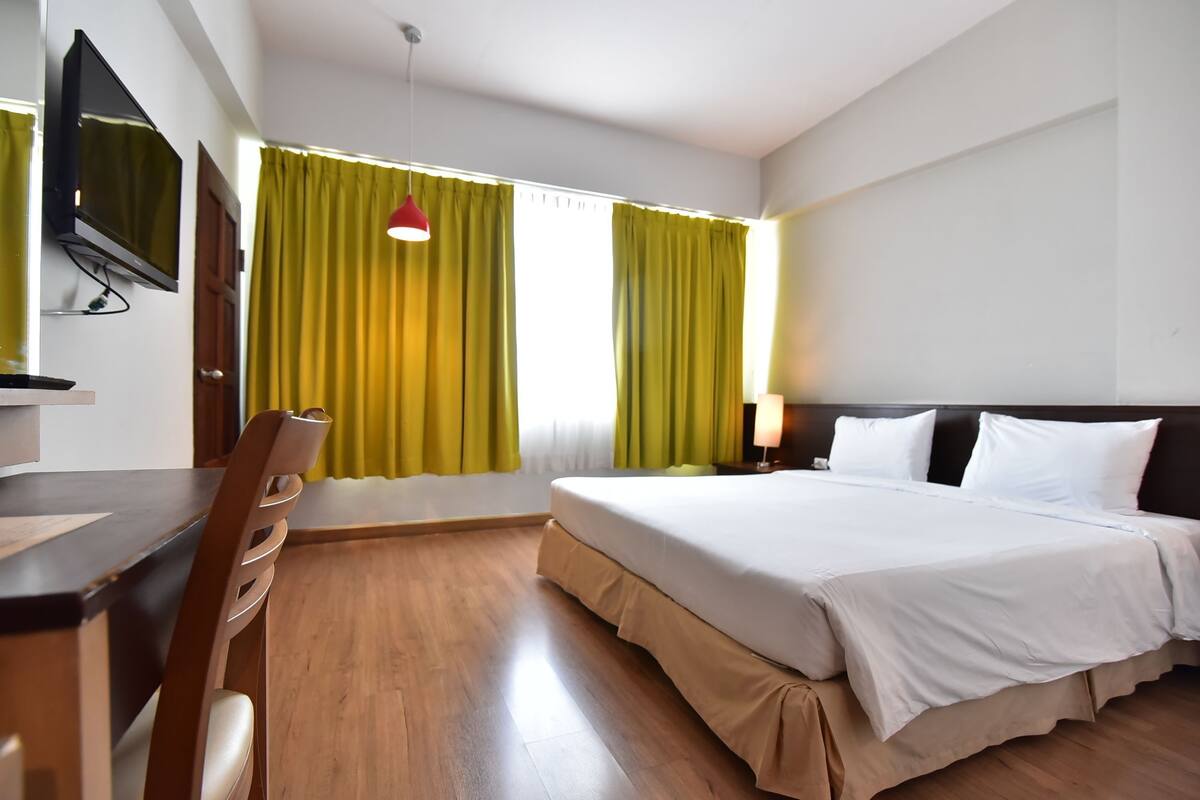 A hotel room with a bed, a desk, a chair, a TV, and curtains.