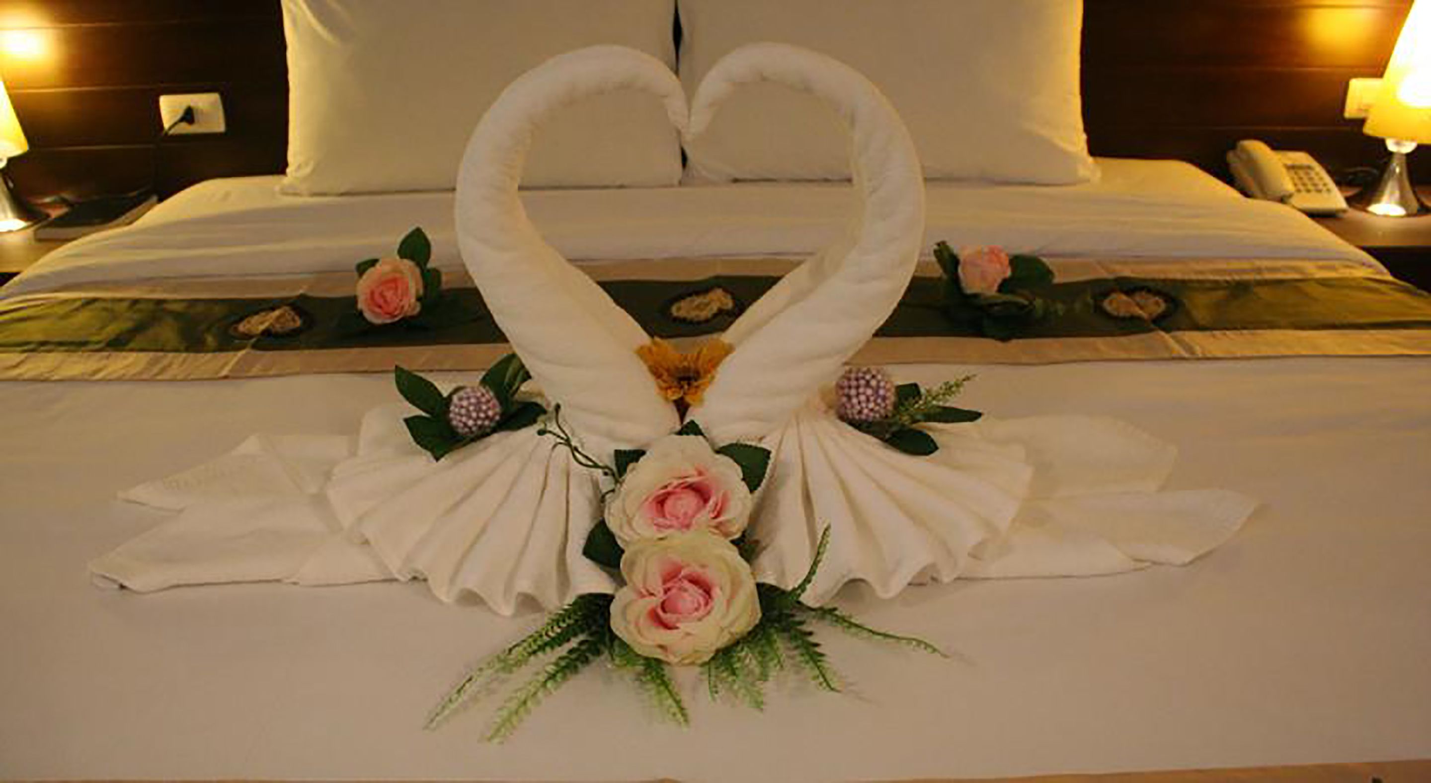 A bed with a heart-shaped towel arrangement and flowers.