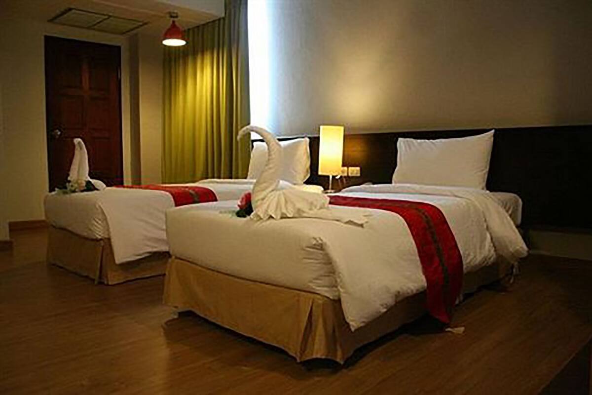 A hotel room with two beds, a red and white bedspread, a lamp, and a curtain.