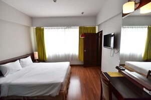 Una habitación de hotel con cama, escritorio, televisión y ventana con cortinas.