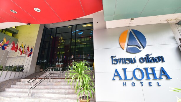 Exterior del Hotel Aloha con diseño moderno, destacando una entrada principal con escalones y una planta en maceta.