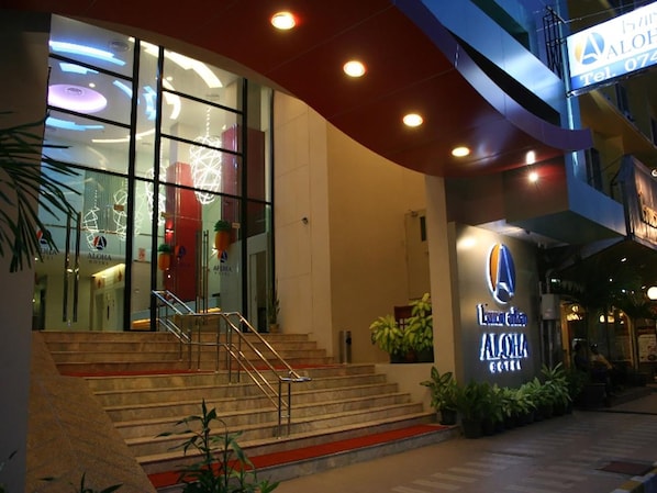 Fachada de hotel de vidrio, con una escalera que conduce a la entrada y un cartel con el nombre del hotel.