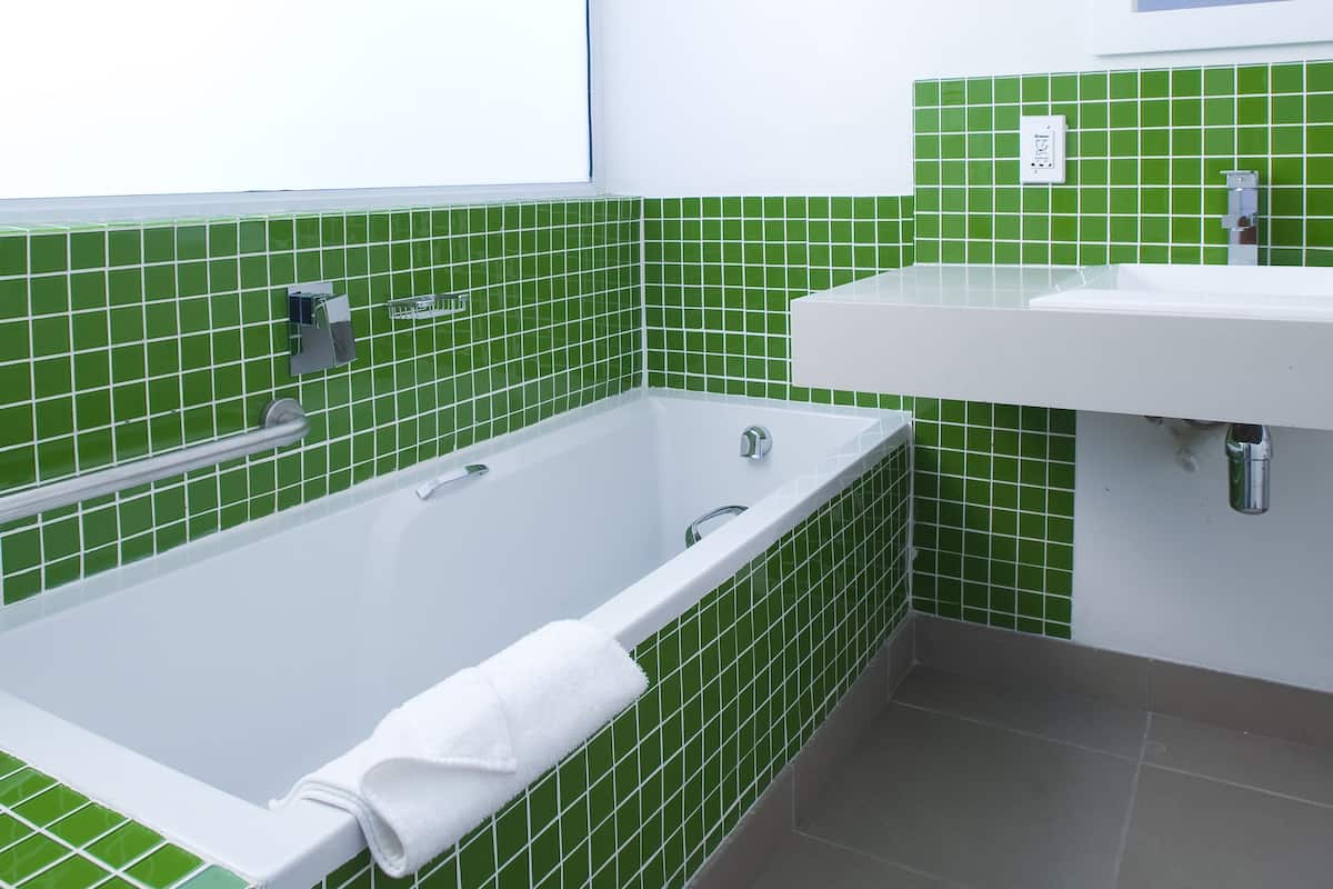 Een badkamer met een muur van groene tegels, een witte badkuip, een witte wastafel en een spiegel boven de wastafel.