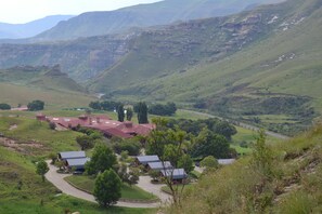 A rural landscape with a cluster of buildings featuring red roofs, surrounded by green hills and a valley. - Golden Gate Hotel (Golden Gate Highlands National Park)