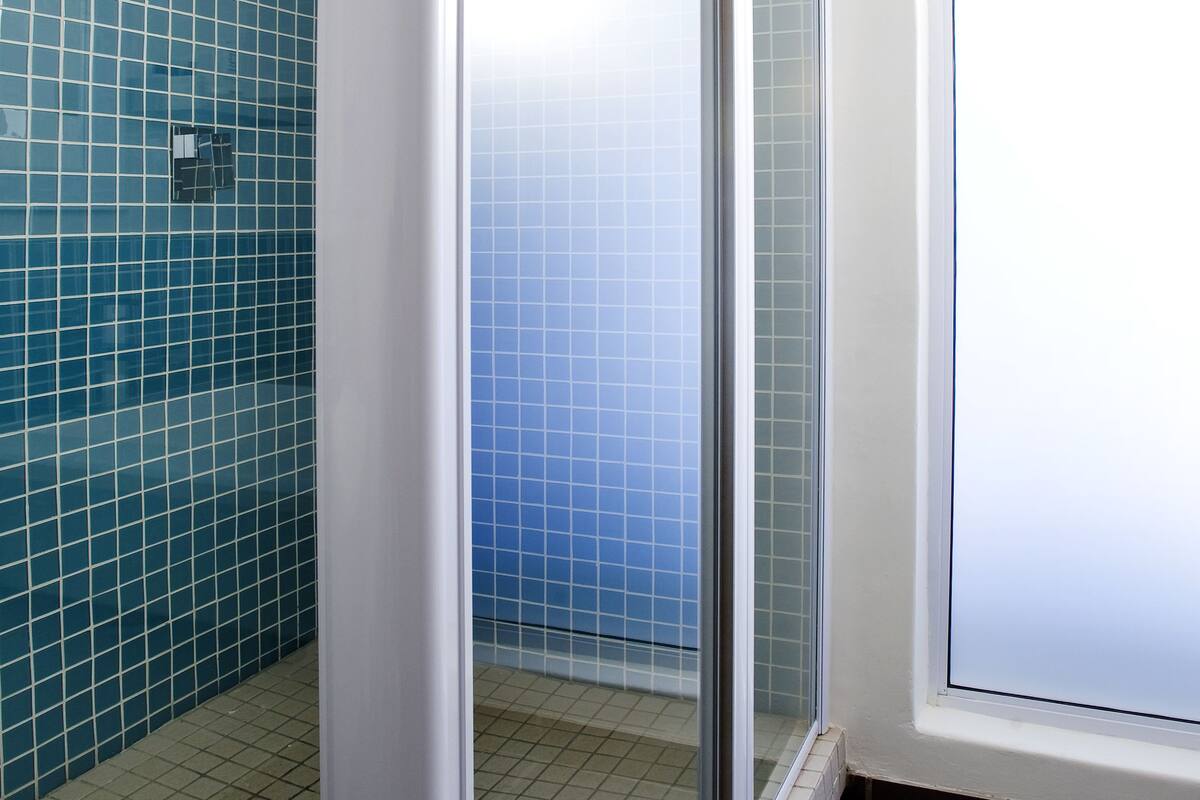 Een badkamer met een glazen douchecabine, betegelde wanden en een raam.