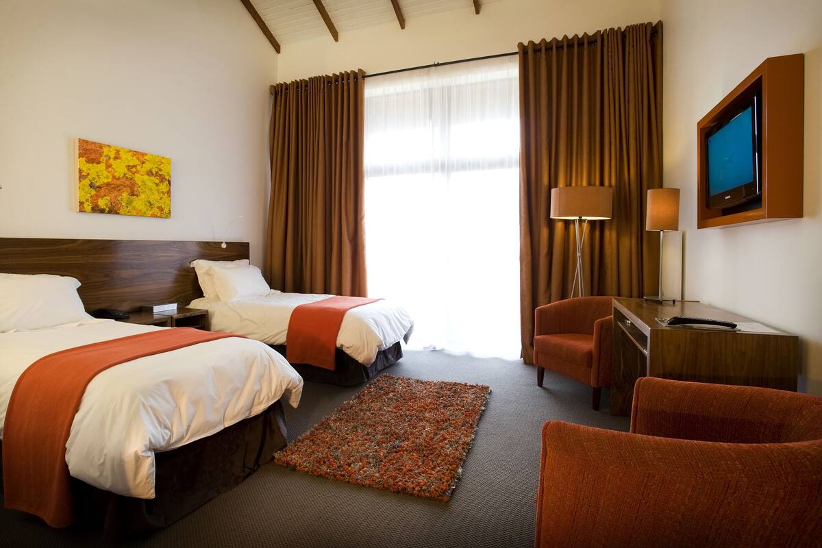 Een hotelkamer met twee bedden, een bureau, een stoel, een televisie en een raam met gordijnen.