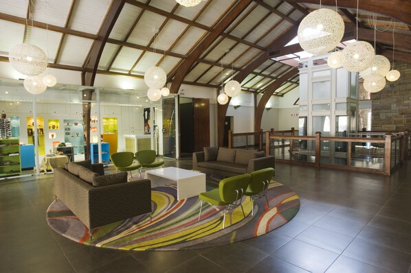 A spacious lobby with a high ceiling, modern furniture, and a large glass wall. - Golden Gate Hotel (Golden Gate Highlands National Park)
