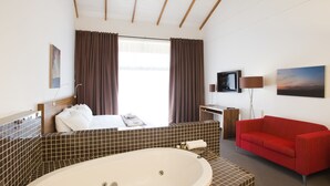 Une chambre d’hôtel avec une grande baignoire, un canapé rouge, une télévision et des œuvres d’art accrochées aux murs.