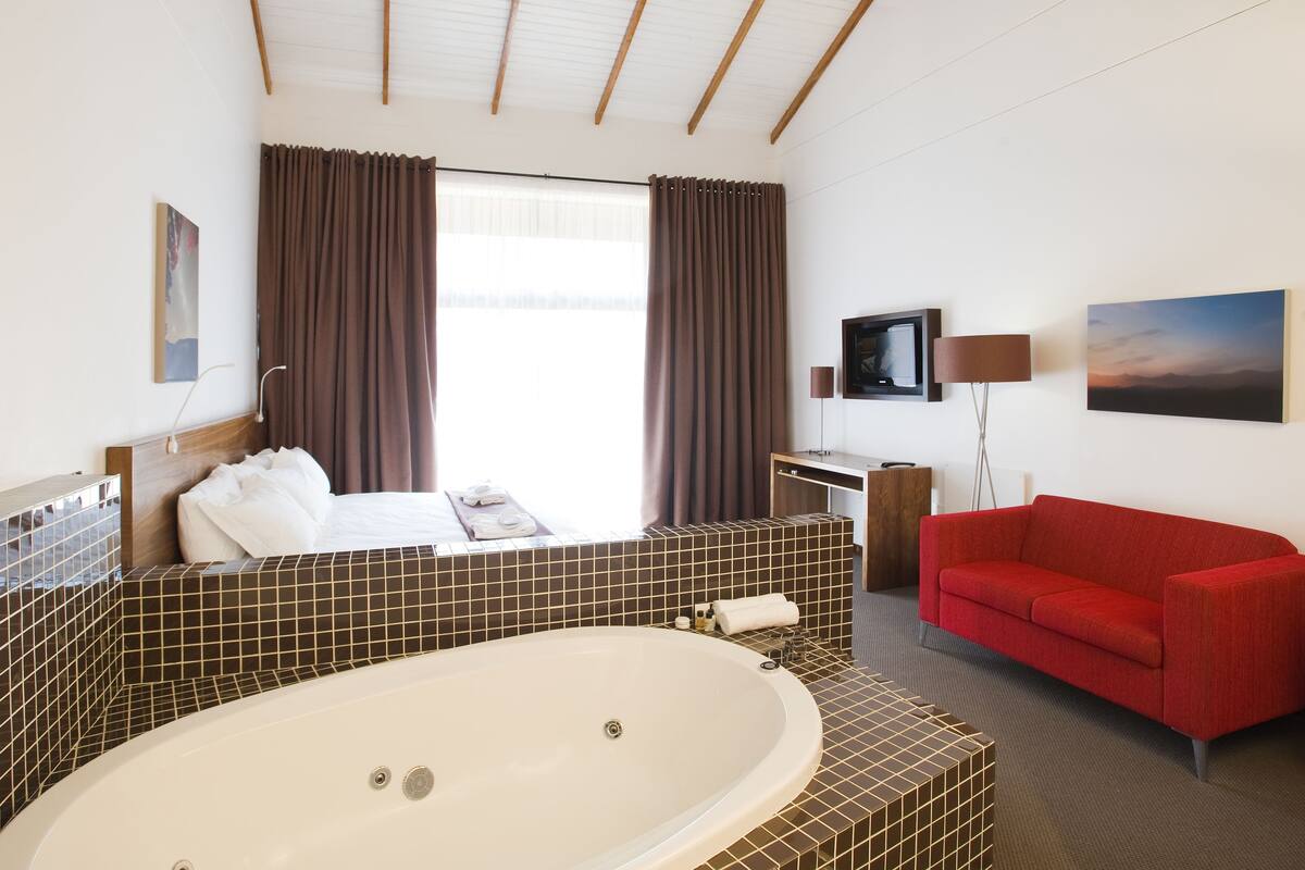 Een hotelkamer met een groot bad, een rode bank, een televisie en kunstwerken aan de wanden.