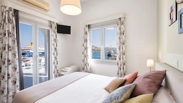 A hotel room with a bed, curtains, a TV, a window with a view of the sea, and a lamp.