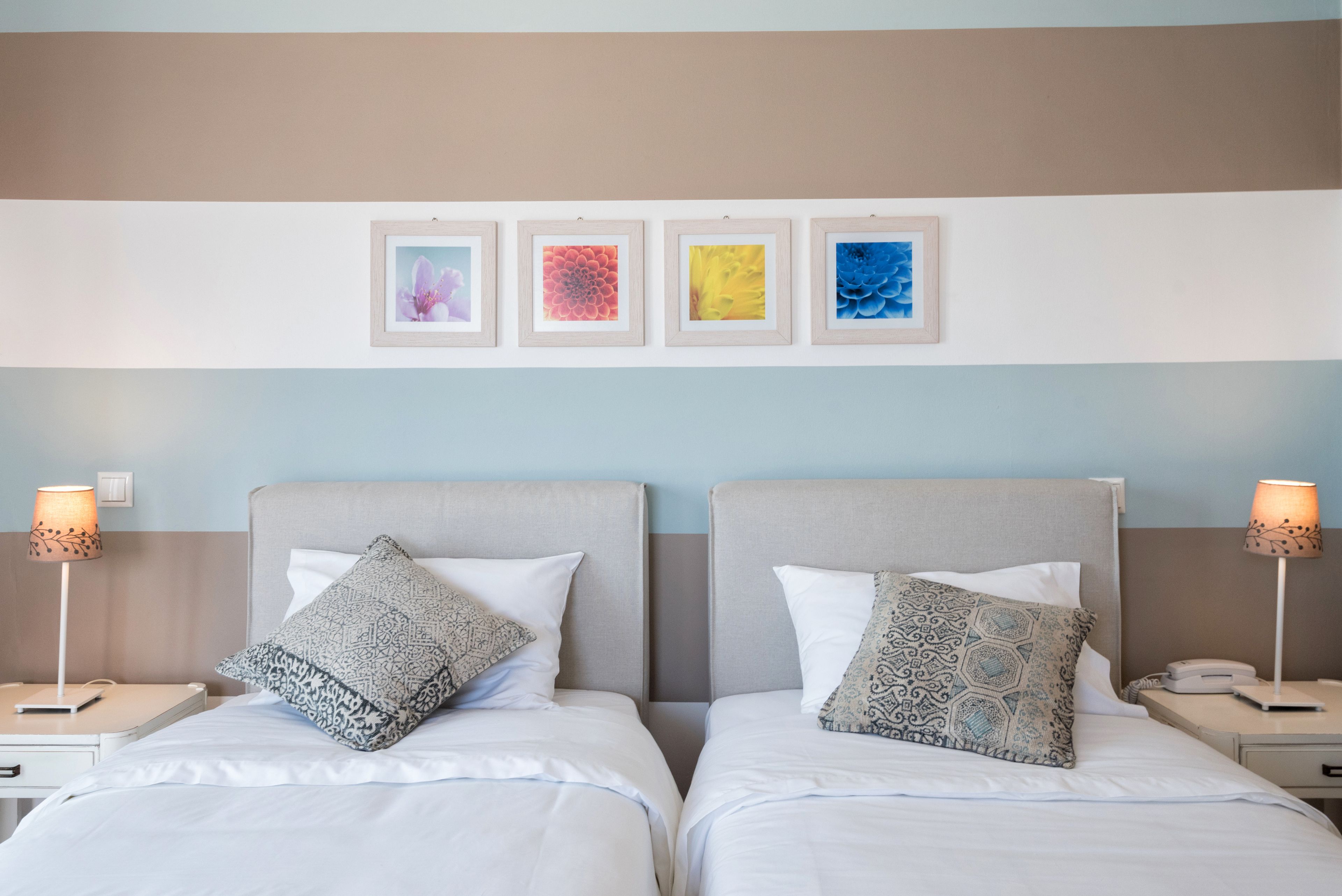 Une chambre d’hôtel avec deux lits, chacun agrémenté d’oreillers à motifs, une table de chevet avec une lampe et un mur orné de quatre œuvres d’art encadrées.