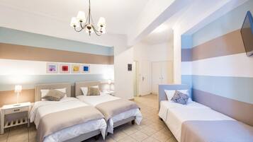 Habitación de hotel con dos camas, un candelabro, una pared con obras de arte coloridas y una puerta que da a otra habitación.
