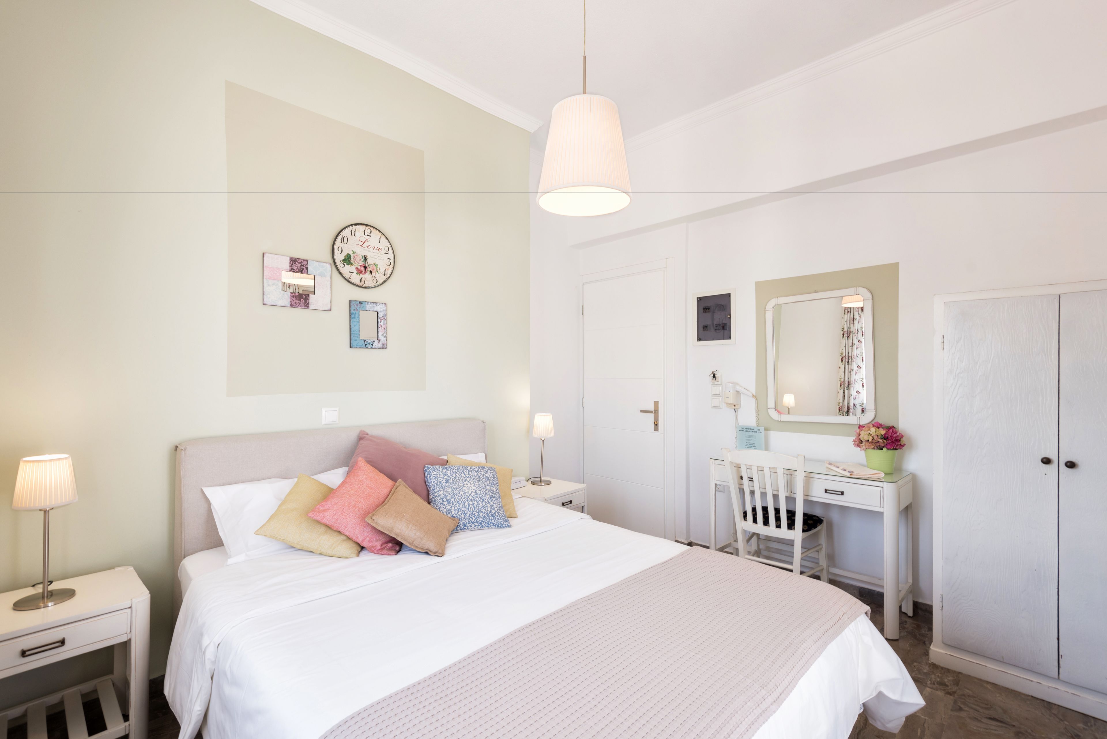 A neatly arranged bedroom with a bed, bedside tables, a dresser, a mirror, and a wardrobe.