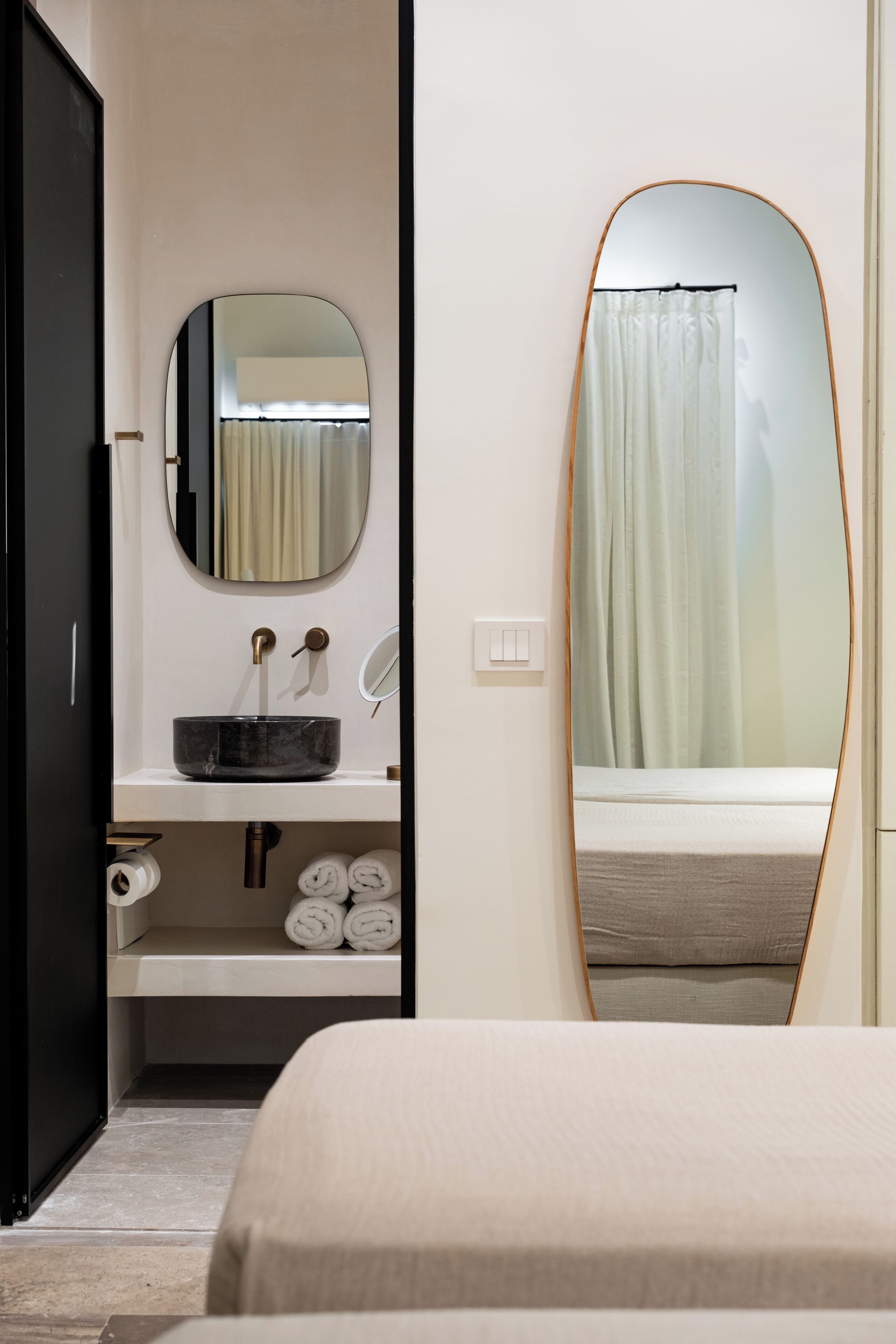 Un baño moderno con un espejo redondo, un lavabo negro y un inodoro.
