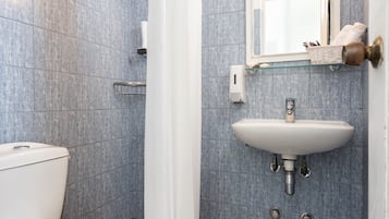 A bathroom with a toilet, a shower with a curtain, a sink, and a mirror.