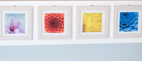 A room with two beds, a wall-mounted light fixture, and four framed floral artworks.