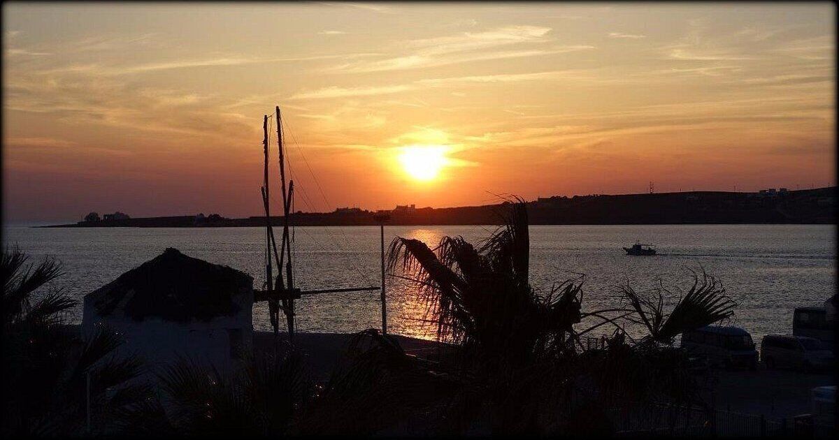Un capvespre sobre una massa d'aigua amb un vaixell, palmeres i una costa llunyana.