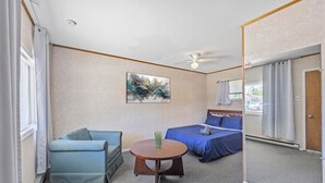 A hotel room with a bed, a sofa, a small table, a ceiling fan, and a painting on the wall.