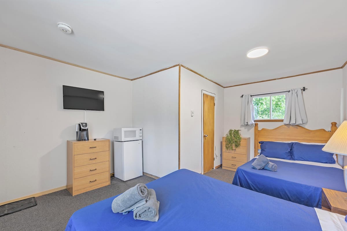 A hotel room with two beds, a TV, a microwave, a wooden dresser, and a window with curtains.