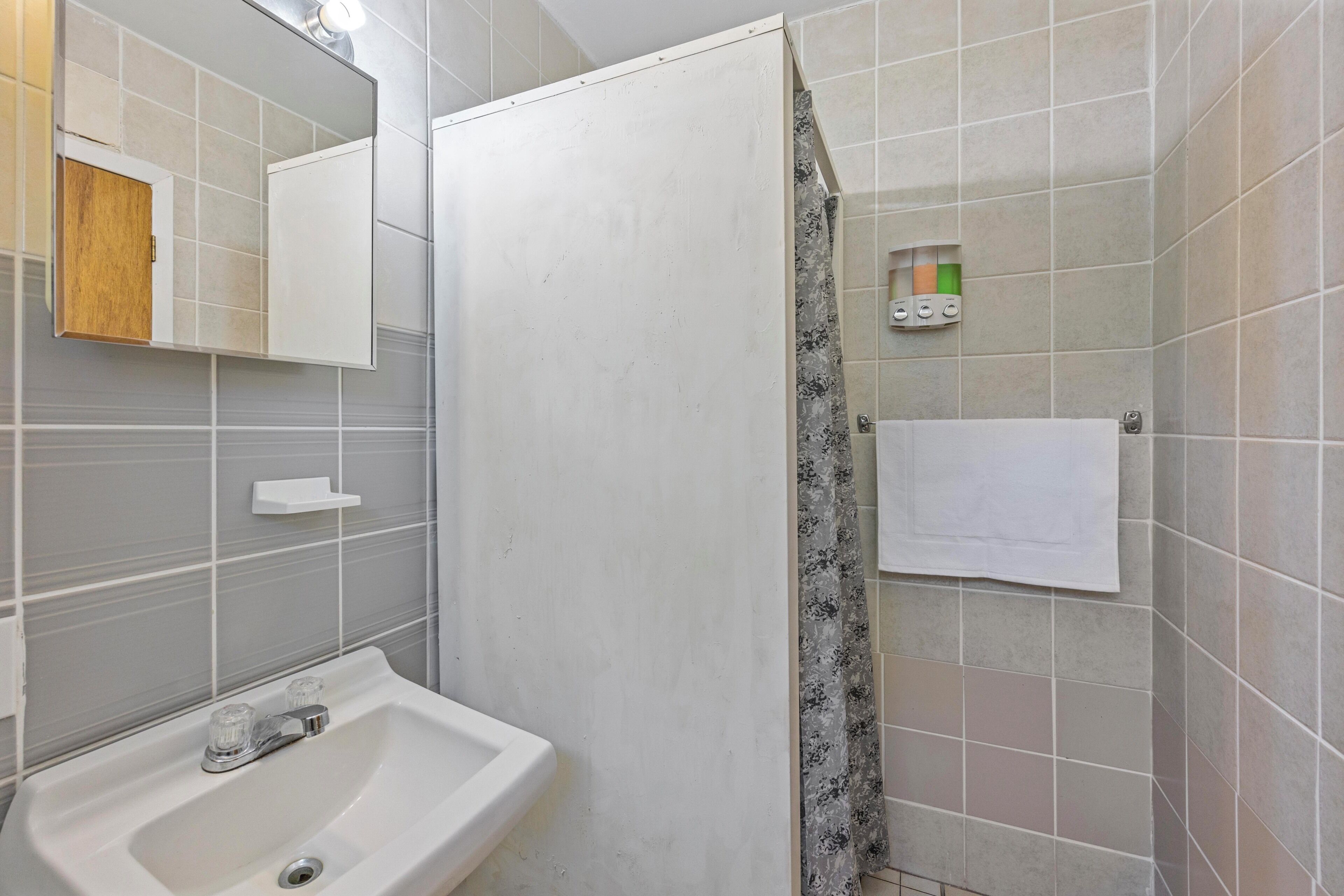 Un baño con lavamanos, espejo, cortina de ducha y toallero.