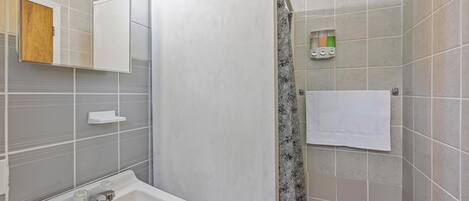 A bathroom with a sink, mirror, shower curtain, and towel rack.