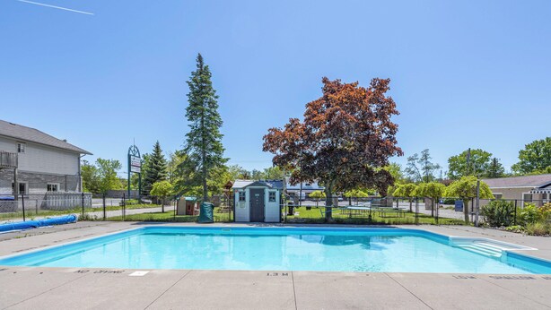 A clear blue swimming pool with a lifeguard tower, surrounded by trees and a fenced area.