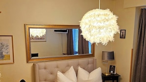 Een slaapkamer met een groot bed, een bureau, een stoel, een spiegel en een hanglamp.