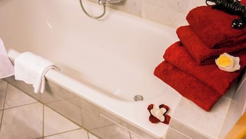 Een bad met douchekop, een handdoek en een rode handdoek met een gele bloem.