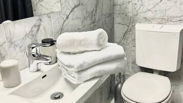 Ein Badezimmer mit Marmorwaschbecken, Toilette und einer Glasablage für Toilettenartikel.