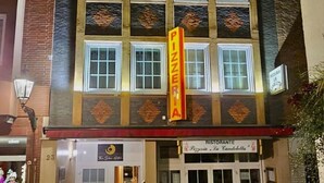 Een gebouw met een pizzeria-bord, een restaurantbord en een deur met een rode loper.