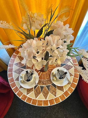 Une table sur laquelle se trouve un vase rempli de fleurs blanches et deux tasses à anse noire.
