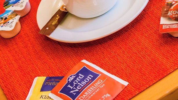 Een ontbijttafel met een kop koffie, een pot honing en een zakje thee.