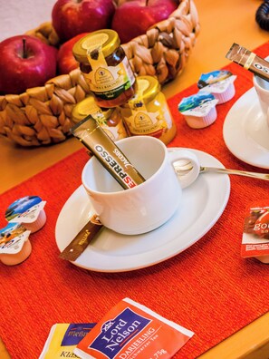 Een ontbijttafel met een kop koffie, een pot honing en een zakje thee.