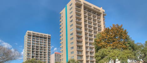A high-rise hotel with multiple floors, balconies, and a parking area with cars.