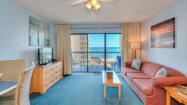 A hotel room with a balcony, a sofa, a TV, a wooden dresser, and a ceiling fan. - The Dunes Towers by Palmetto Vacations (Myrtle Beach)