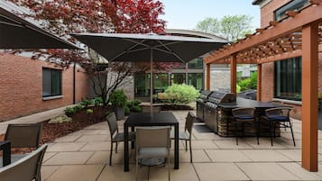 A patio area with a table and chairs, a grill, and a pergola structure.
