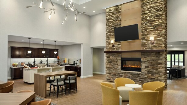 A spacious living area with a stone accent wall, a fireplace, and modern furniture. - Homewood Suites by Hilton Burlington (South Burlington)
