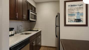 Una cocina compacta con armarios de madera oscura, un microondas de acero inoxidable, un lavamanos doble y un lavavajillas.